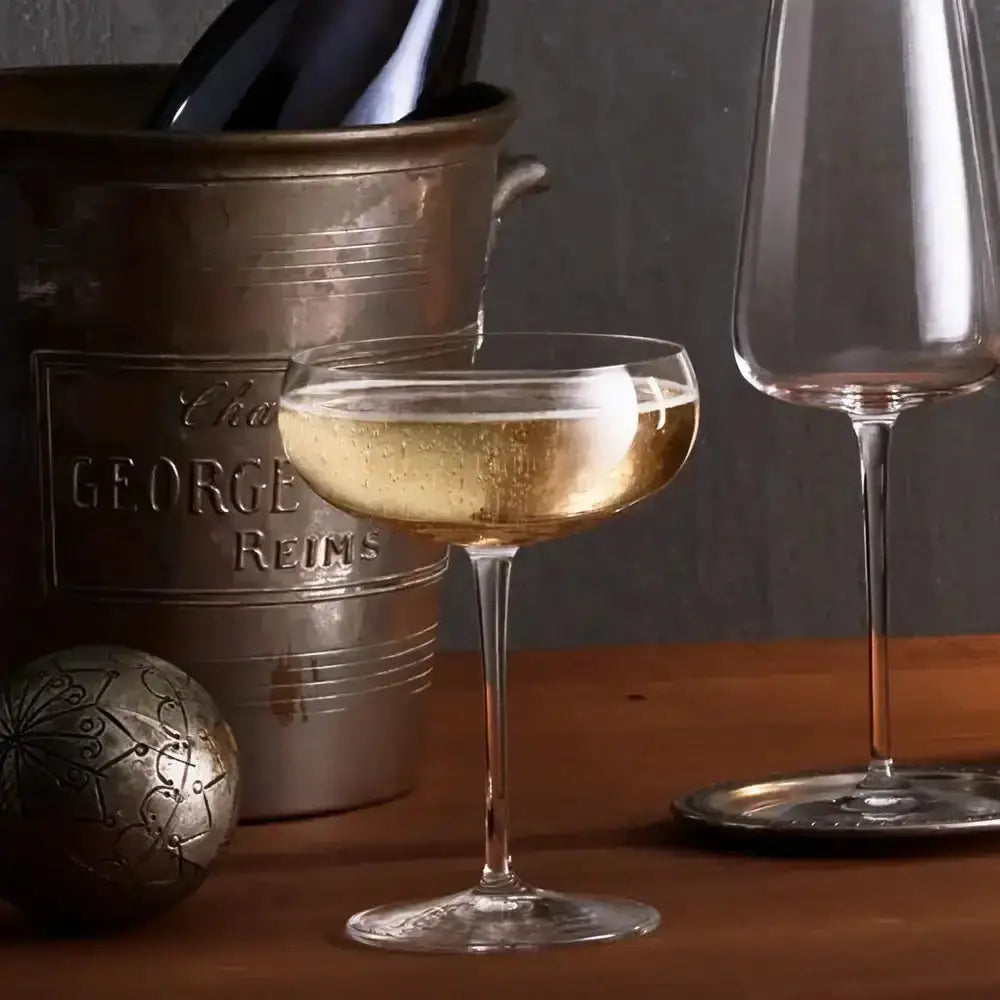 Wine glass with a drink next to a wine bottle in an ice bucket on a wooden surface.