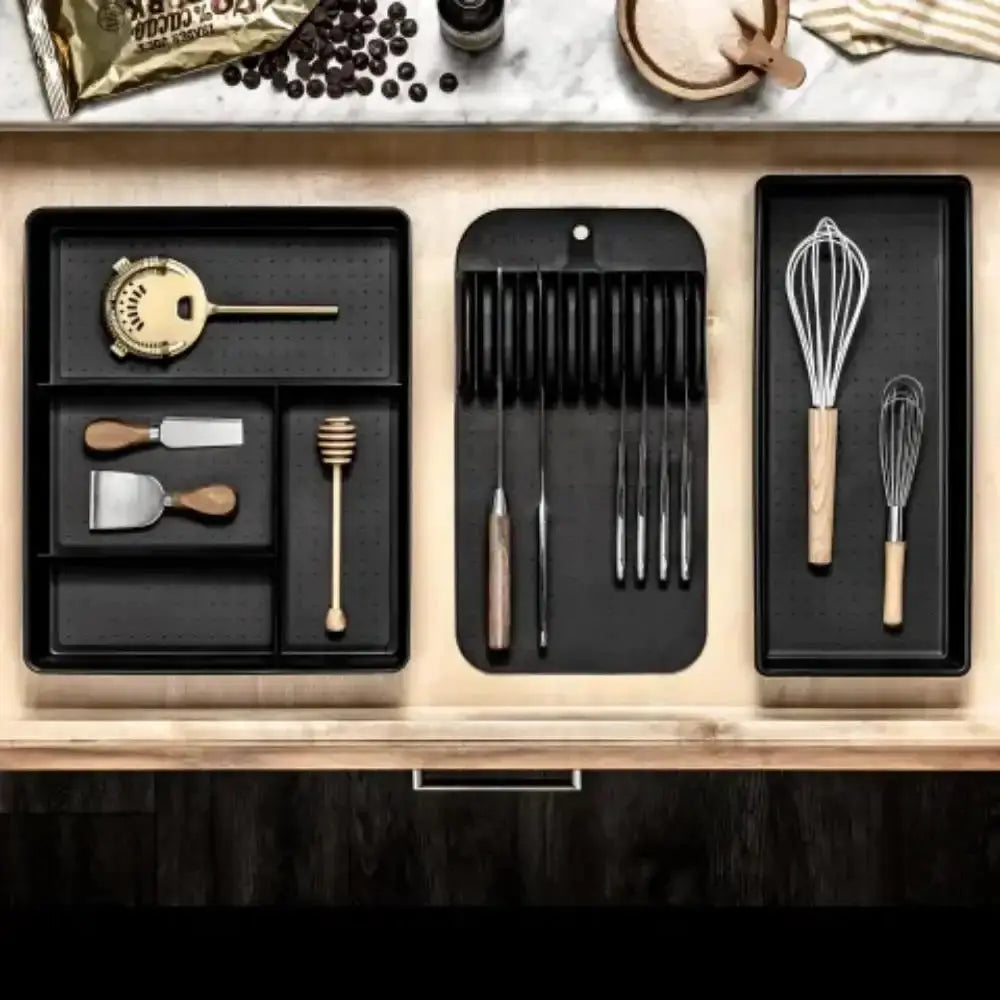 Set of kitchen utensils in black trays on a wooden surface with a marble background.