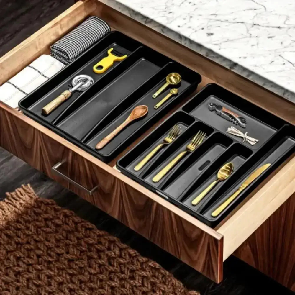 Open wooden drawer with black cutlery organizer containing gold and silver utensils.