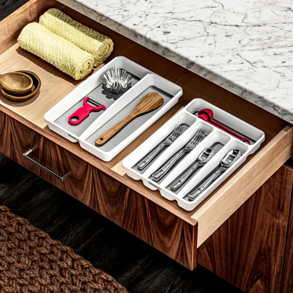 Wooden drawer with organized cutlery and kitchen tools on a marble countertop.