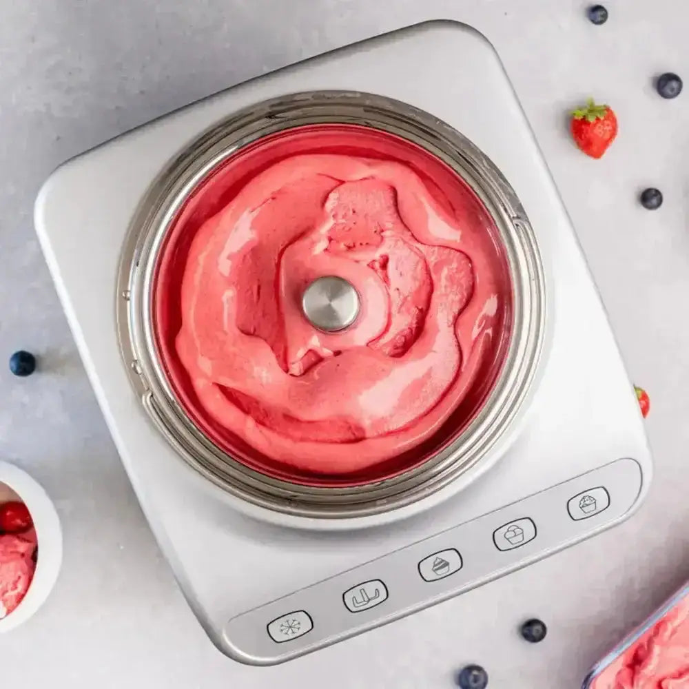 Pink ice cream in a portable ice cream maker with berries around on a light gray background