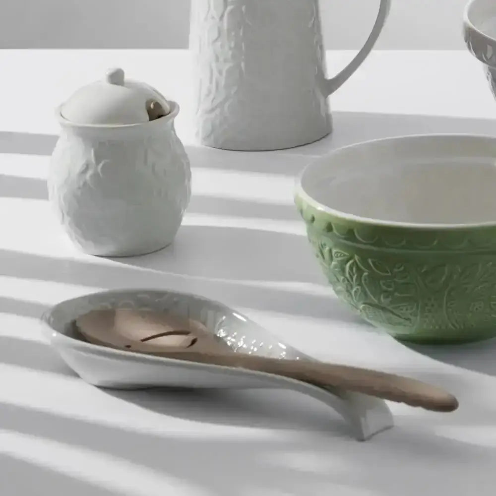 White ceramic mason cash in the forest spoon rest holding a wooden handled metal spoon for kitchen use