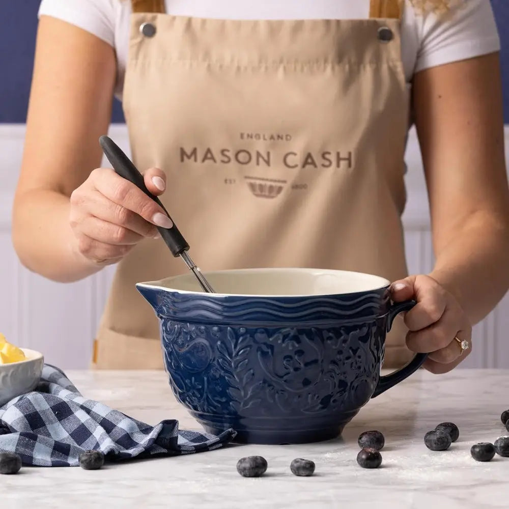 Person wearing a Mason Cash apron using a blue mixing bowl with a spoon.