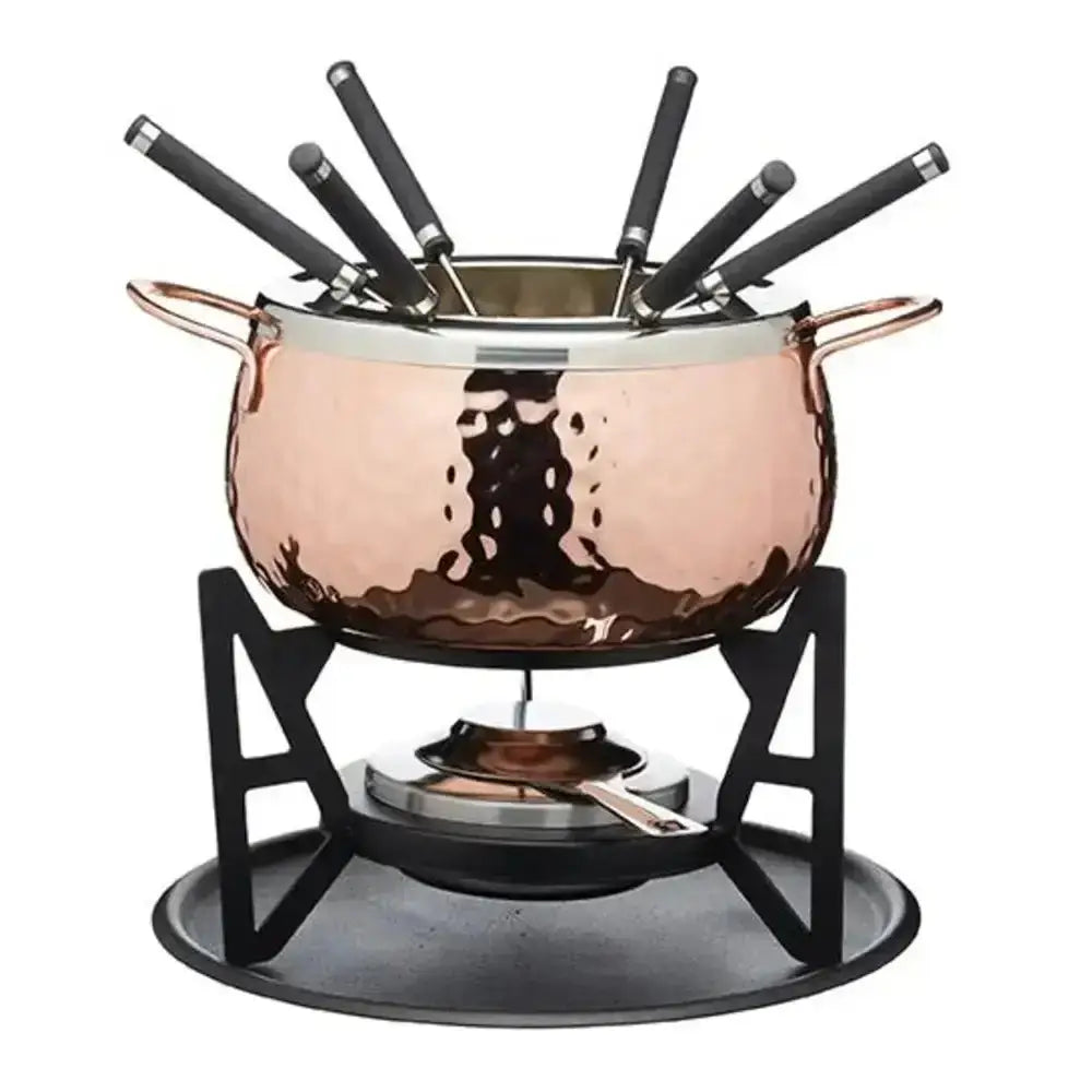 Copper fondue pot with black utensils on a white background