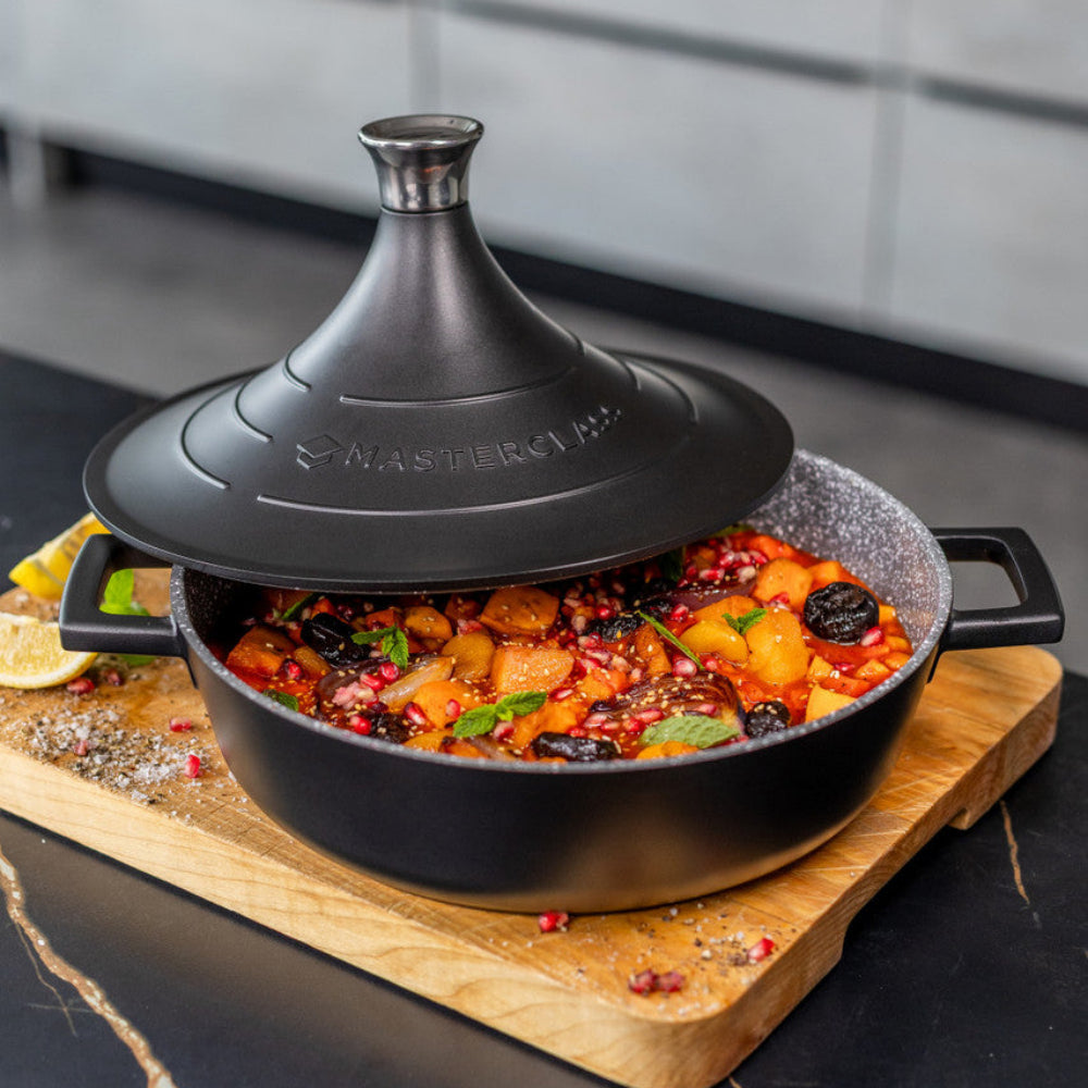 Black tagine with food on a wooden board in a kitchen setting