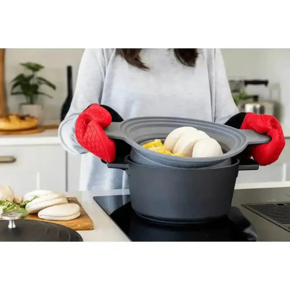 Person holding a stack of gray silicone bowls with red oven mitts in a kitchen setting.