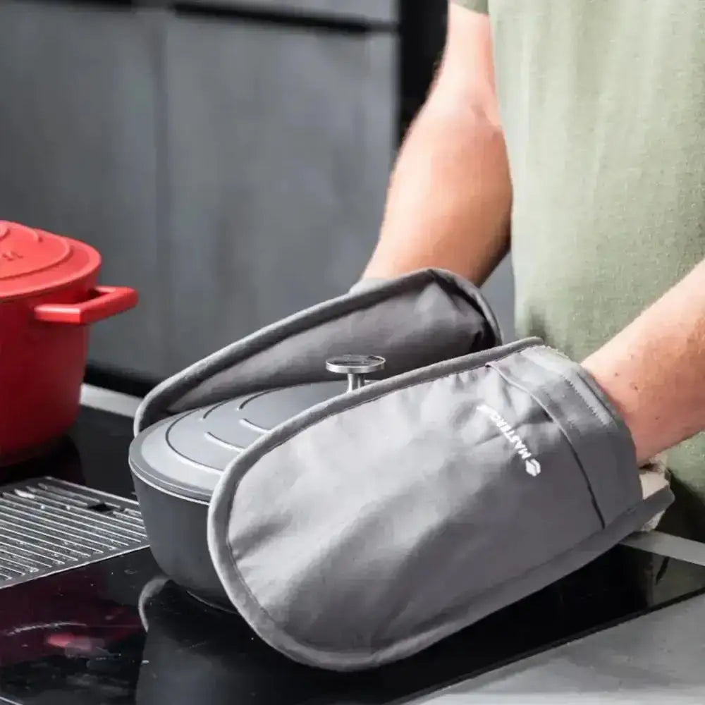 Person wearing gray oven mitts holding a small gray container on a stove.