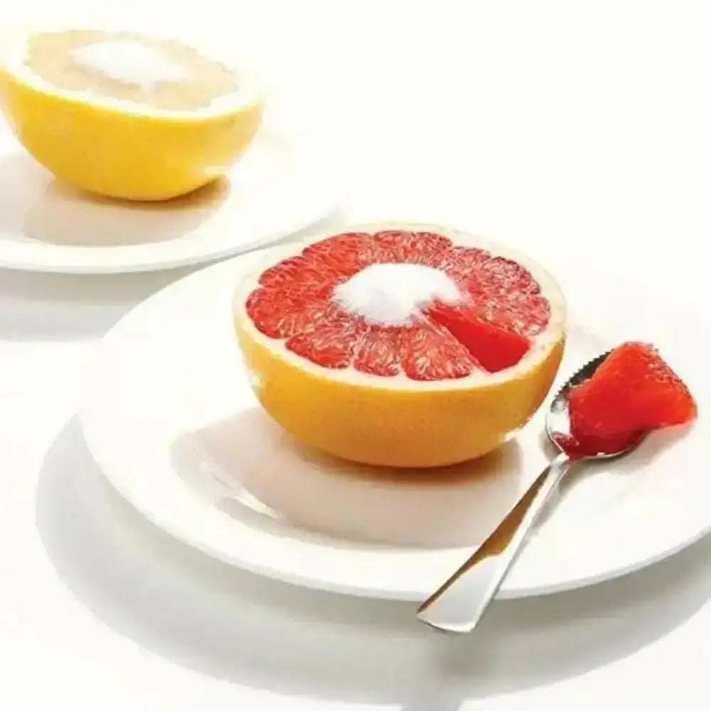 Half of a grapefruit on a white plate with a spoonful of grapefruit on a white background