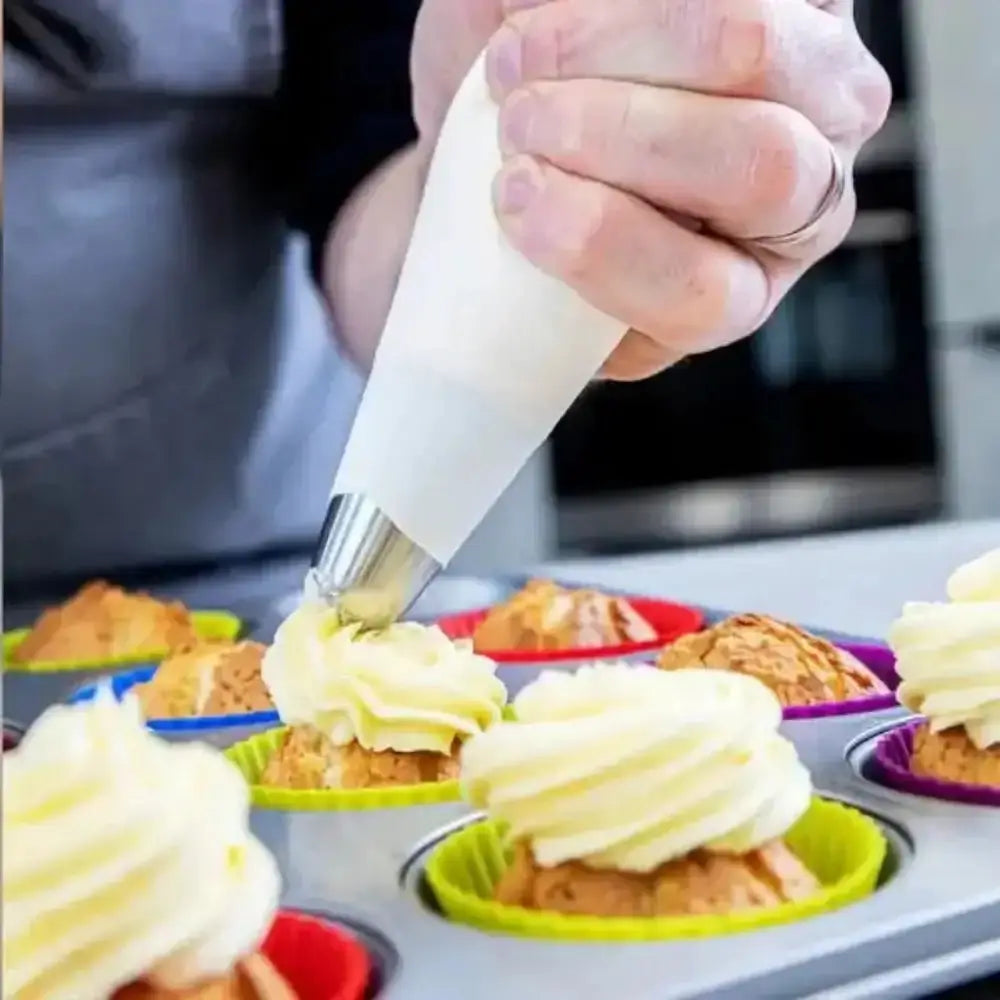 Person frosting cupcakes in a baking tray with colorful cupcake liners.