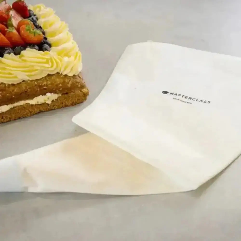 Pastry bag with 'Masterclass' branding next to a cake with fruit and cream on a gray surface