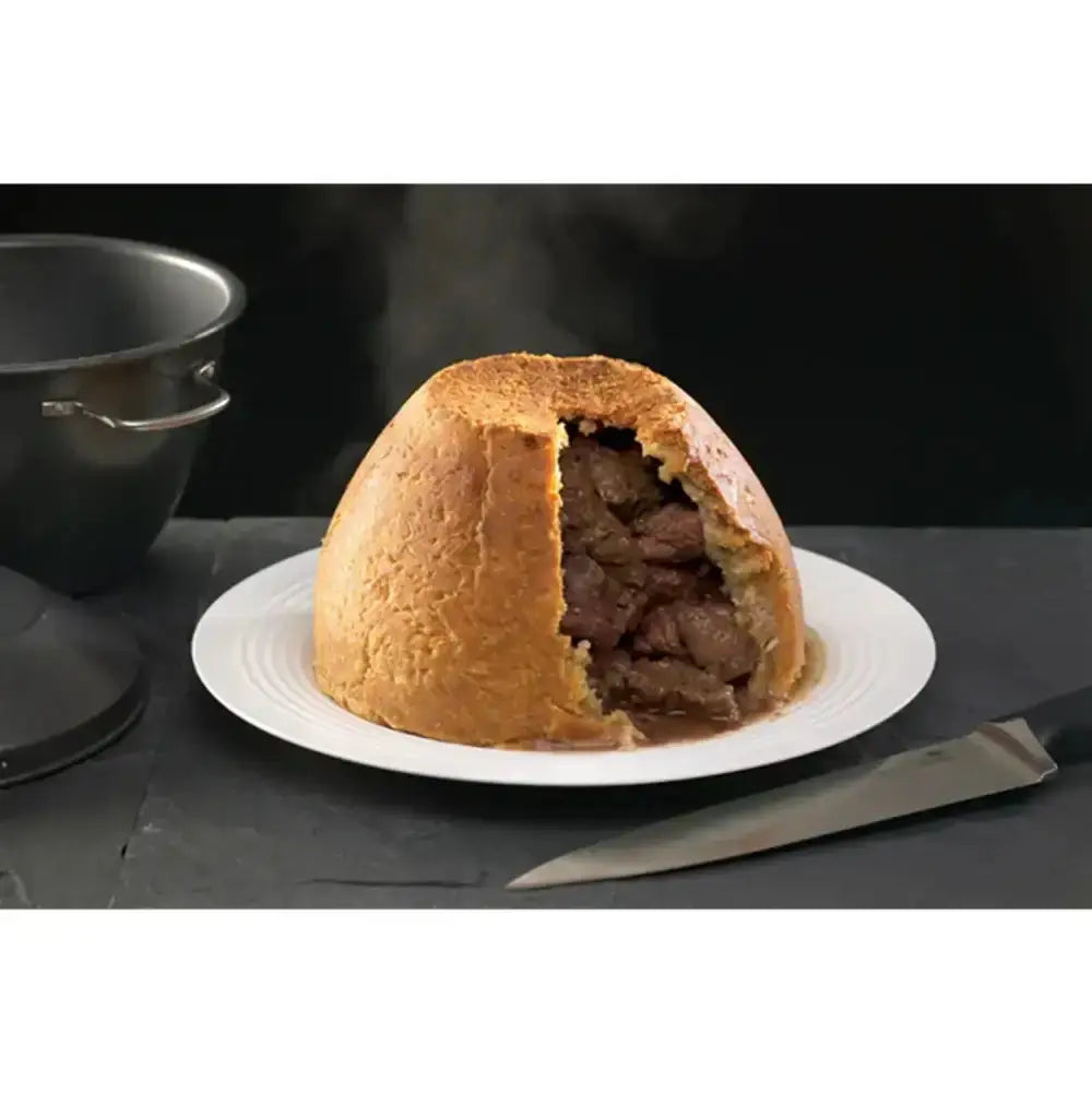 Steamed pudding with meat filling on a white plate, knife nearby