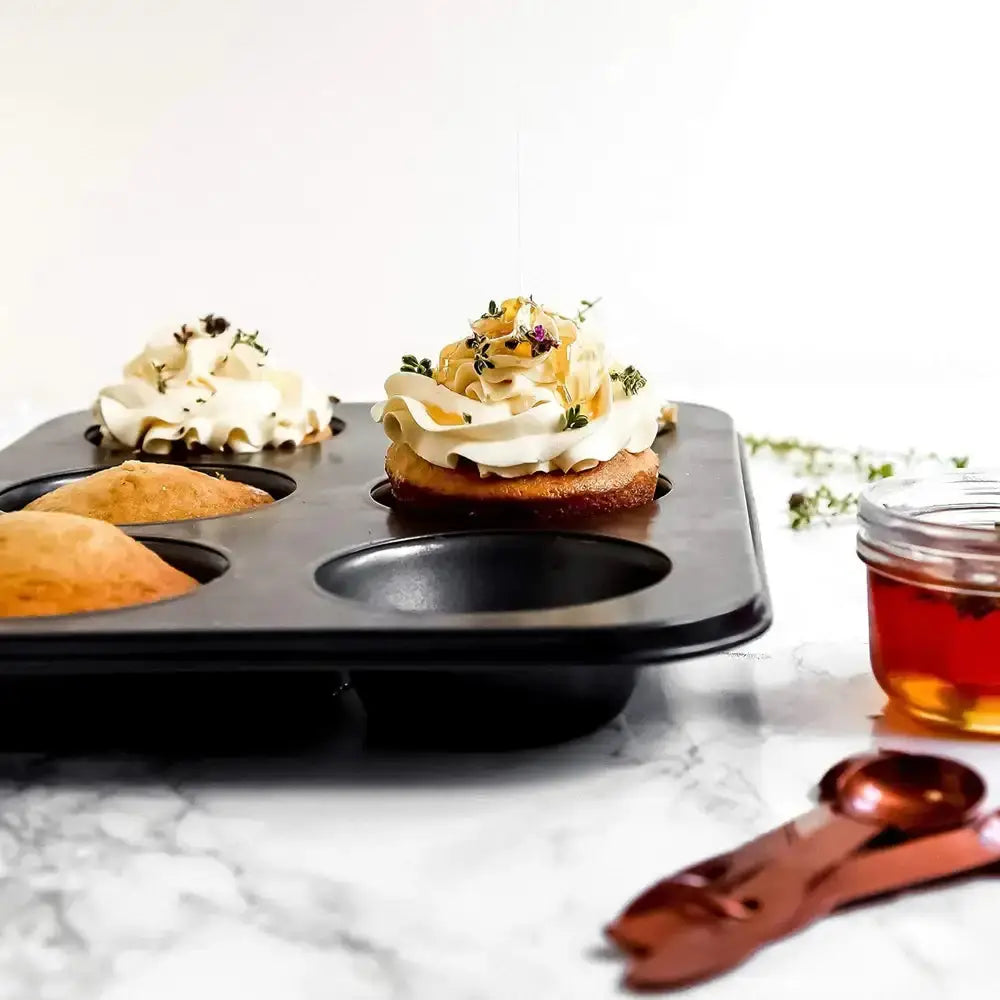 Muffin tin with cupcakes on a marble surface, accompanied by a jar of jam and measuring spoons.