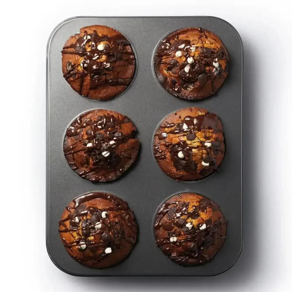 Six brownies with chocolate drizzle in a muffin tin on a white background