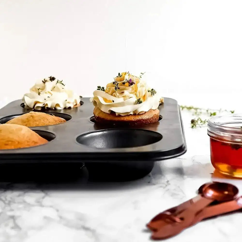 Muffin tin with cupcakes on a marble surface, accompanied by a jar of jam and measuring spoons.