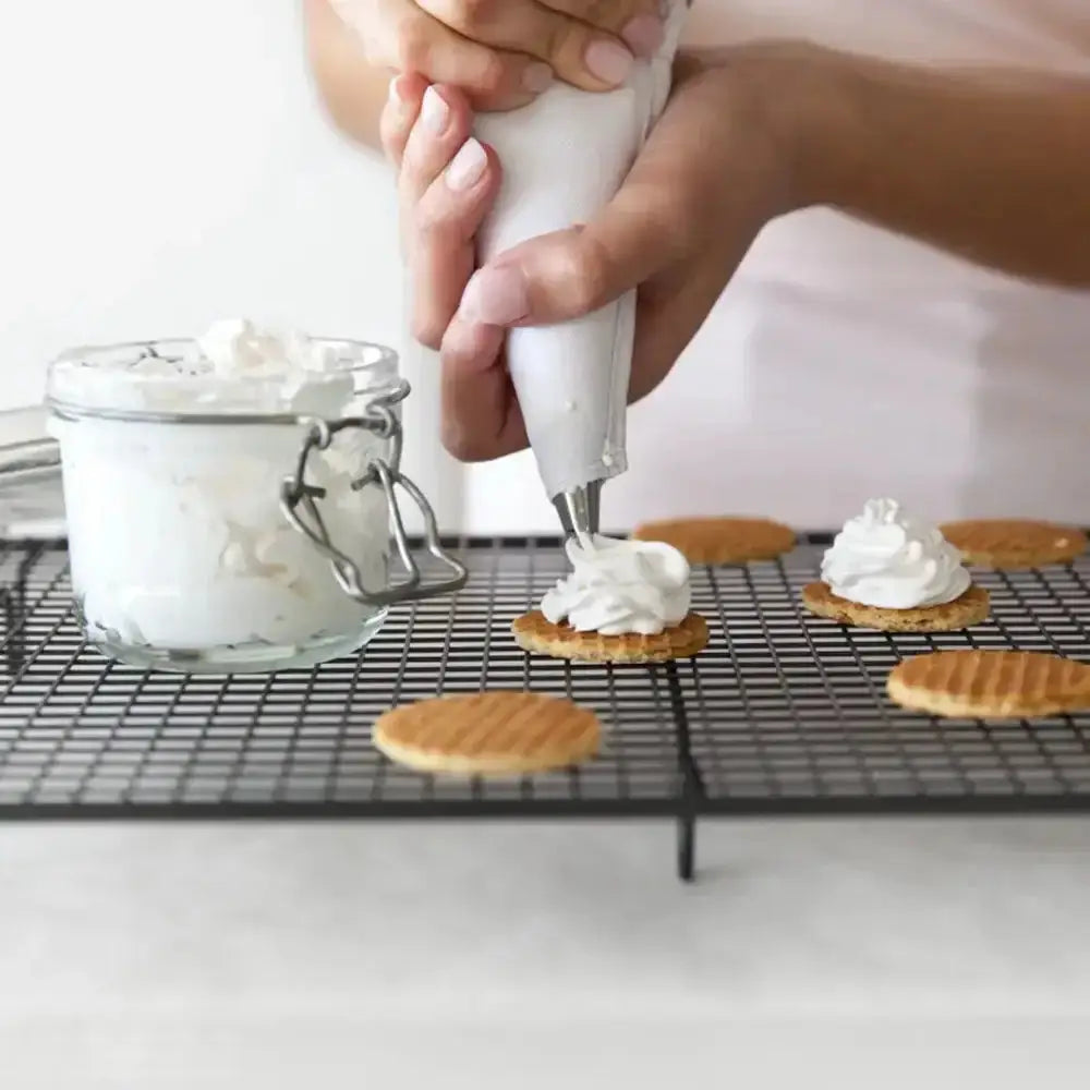 Person using a piping bag to decorate cookies with cream on a cooling rack.