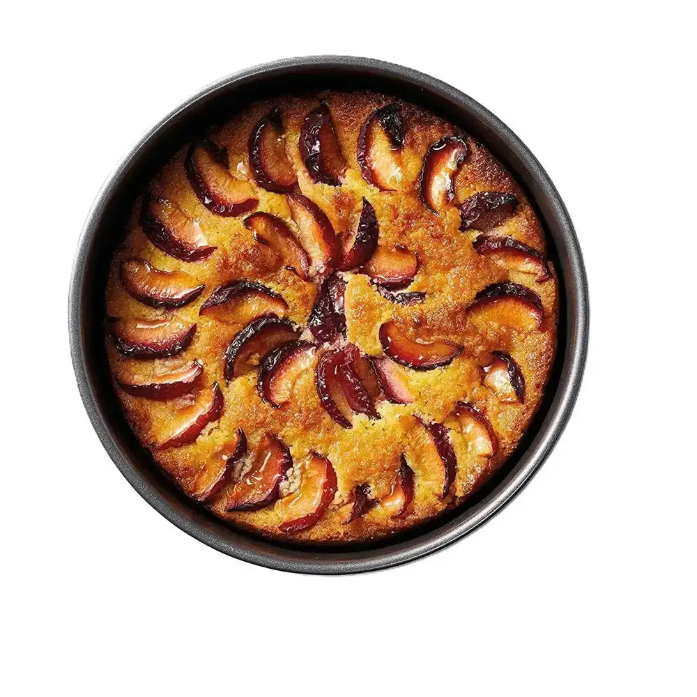 Baked cake with plum slices in a round baking pan on a white background