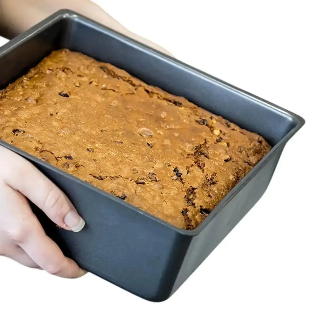 Loaf of bread in a baking pan held by a hand on a white background