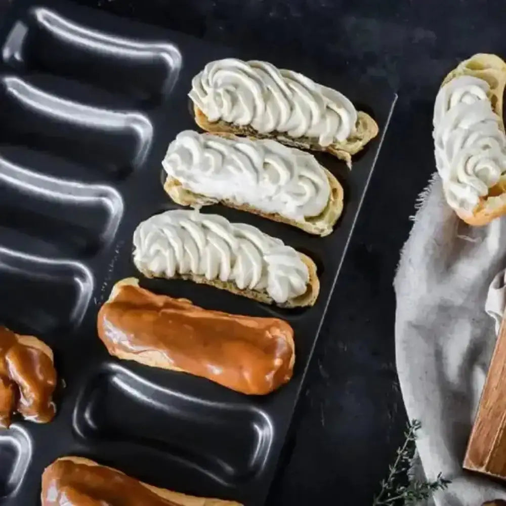 Eclairs with white cream on a black tray with a dark background