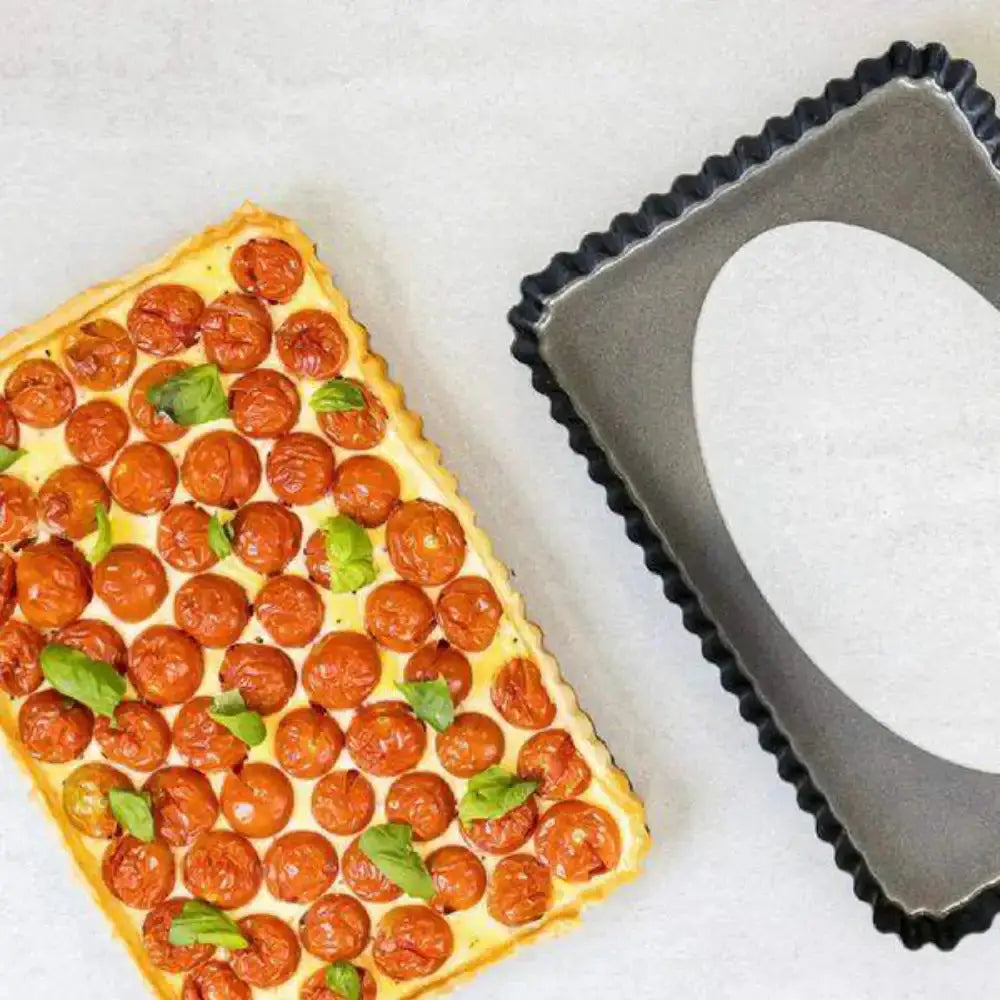 Rectangular tart with cherry tomatoes and basil leaves next to a metal tart pan.