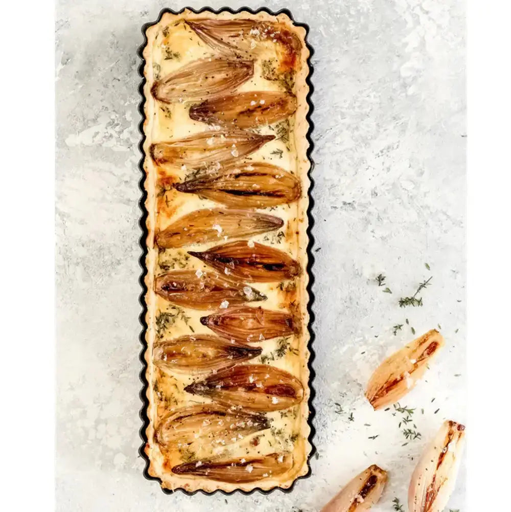 Long rectangular tart with sliced onions on a textured surface