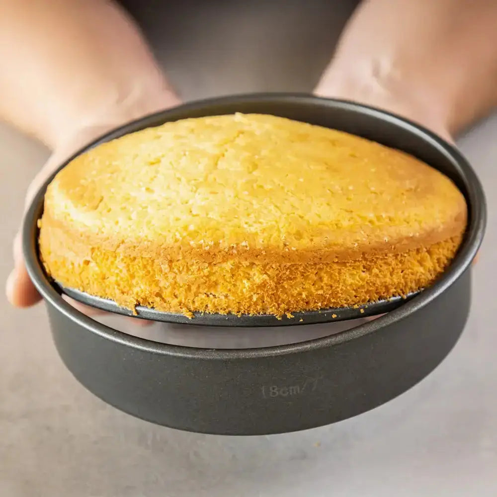 Baked cake in a round metal baking pan held by a person.