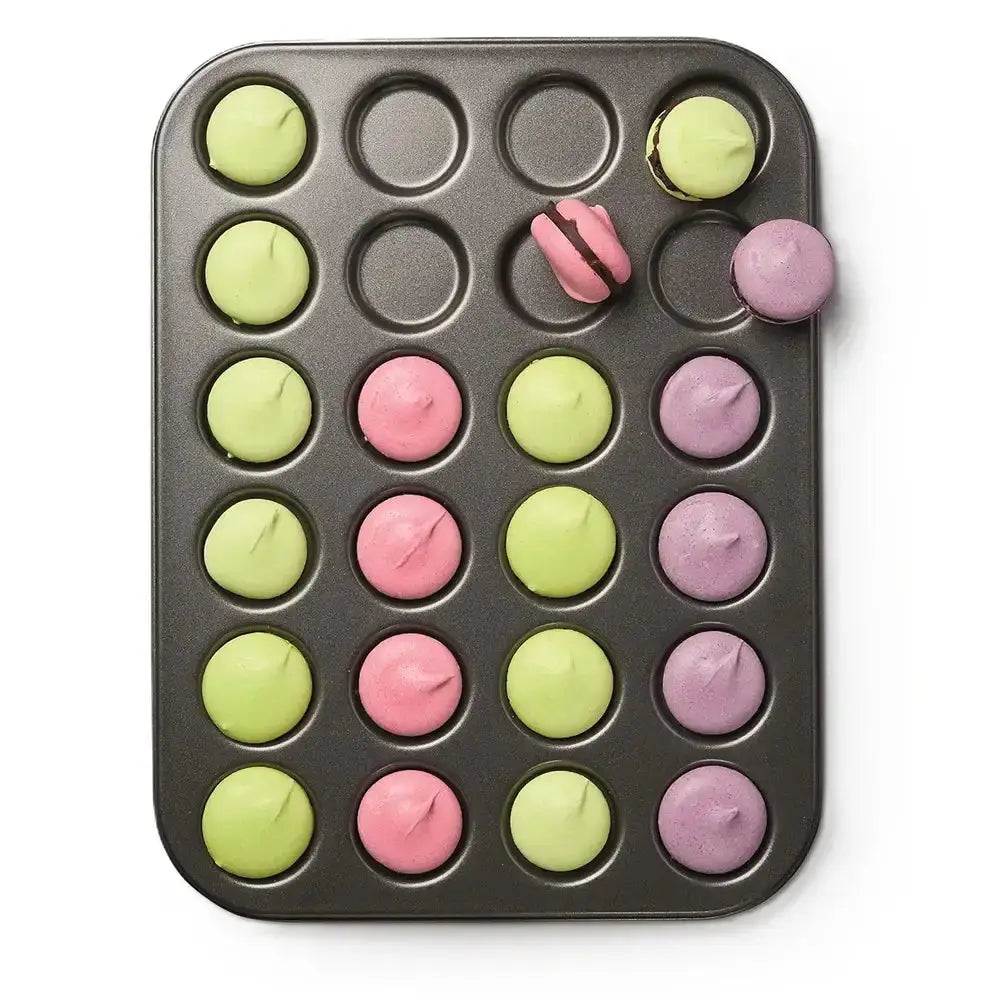 Muffin tin with colorful macaron batter on a white background