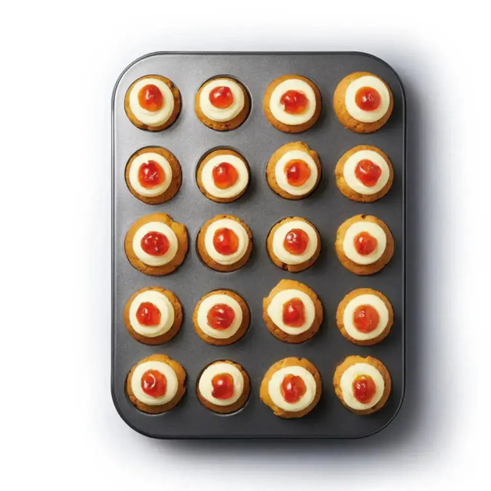 Baking tray with round baked goods topped with cream and red jelly on a white background