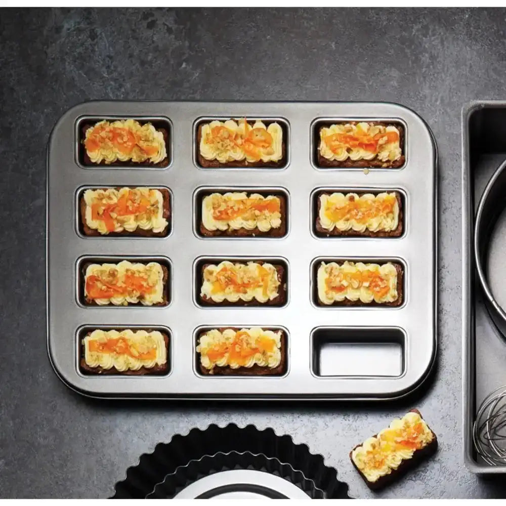 Baking tray with small rectangular compartments filled with a mixture on a dark surface.