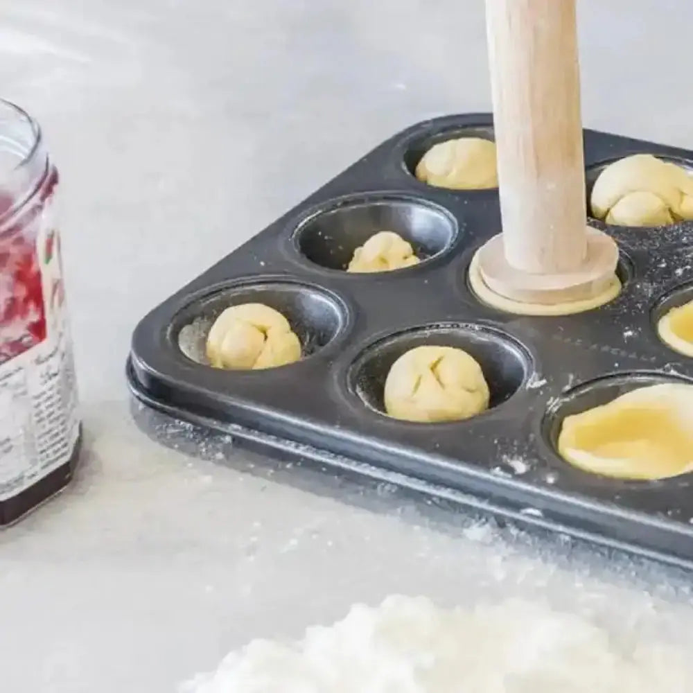 Bread dough being shaped into loaves in a muffin tin with a wooden roller.