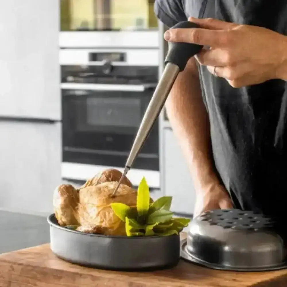 Person using a kitchen tool to check the doneness of a roasted chicken in a kitchen setting.