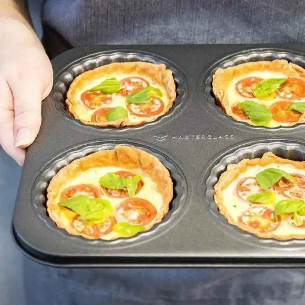 Muffin tin with mini pizzas topped with tomatoes and basil