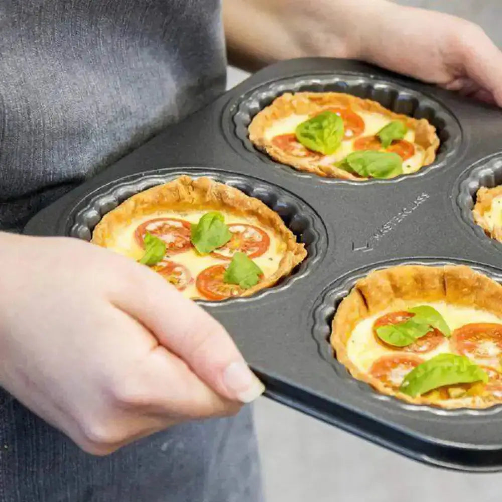 Person holding a muffin tin with small pizza-like dishes topped with tomatoes and basil.