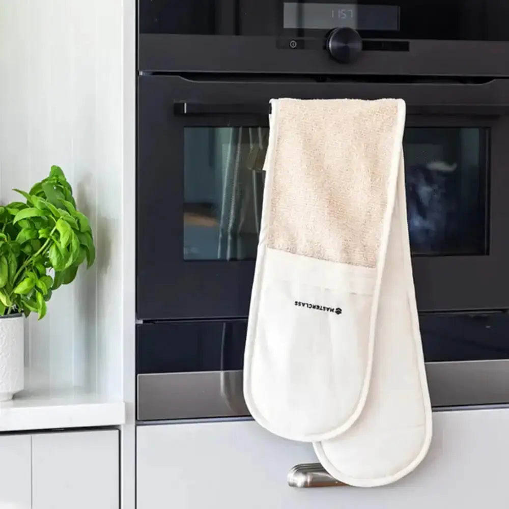 Beige oven mitt hanging in front of a black oven in a kitchen setting.