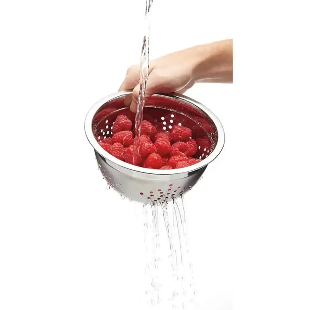 Hand washing raspberries in a metal colander with water flowing over them on a white background