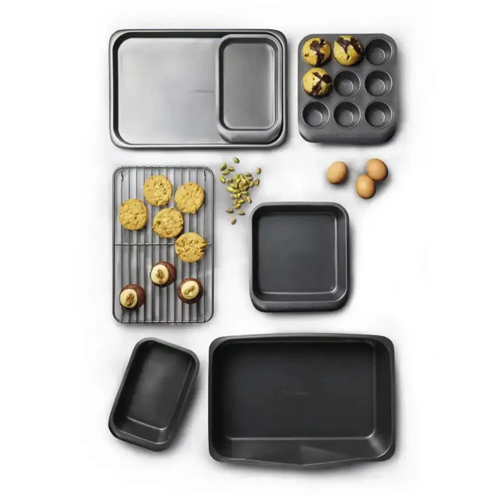 Collection of black baking trays and pans with baked goods on a white background