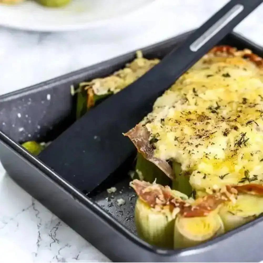 Stuffed zucchini boats with cheese and herbs in a baking dish with a spatula.