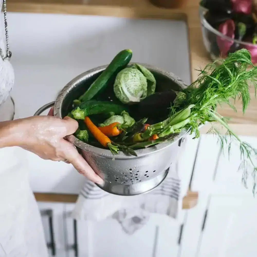 Colander with vegetables held by a hand on a kitchen counter