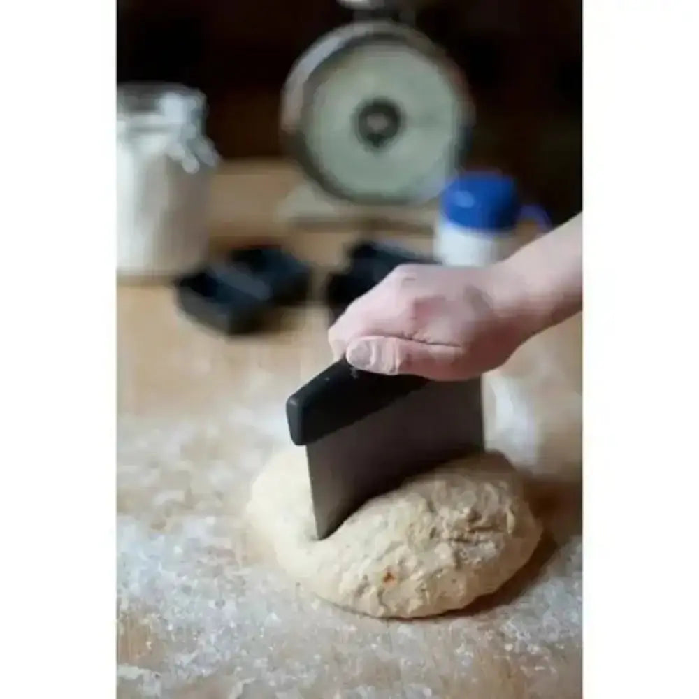Person using a dough scraper on a floured surface with kitchen items in the background