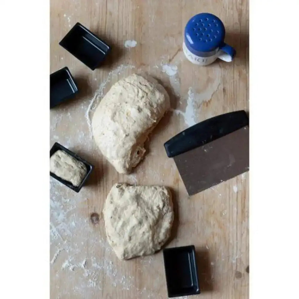 Two pieces of dough on a wooden surface with baking tools.