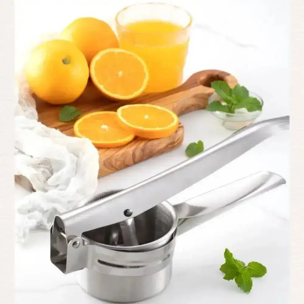 Stainless steel manual juicer with oranges and a glass of juice on a white background