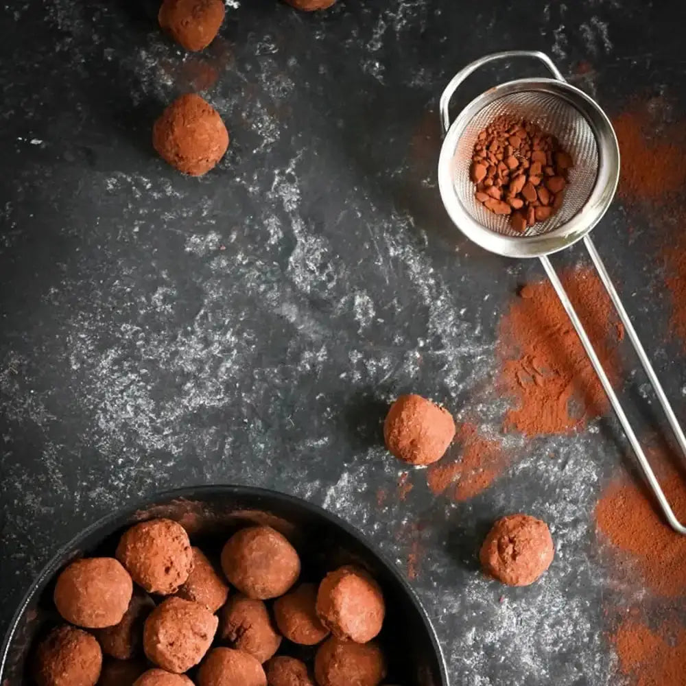 Chocolate truffles with a sifter of cocoa powder on a dark surface