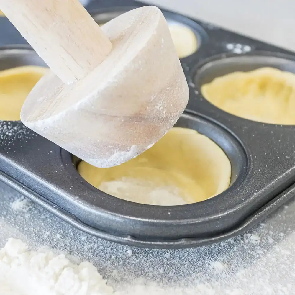 Wooden mallet pressing dough into a muffin tin