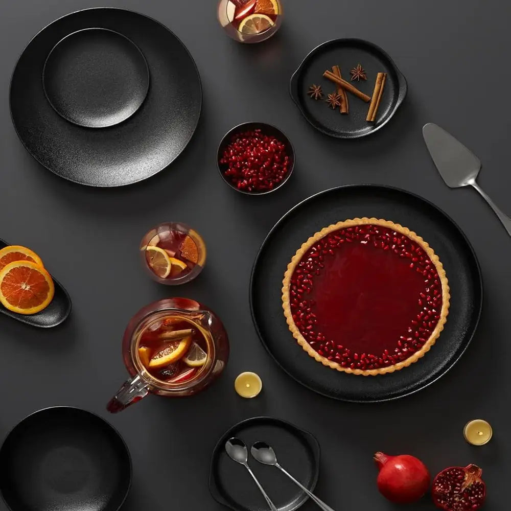 Dark table setting with a tart, glasses of orange juice, and pomegranate seeds.