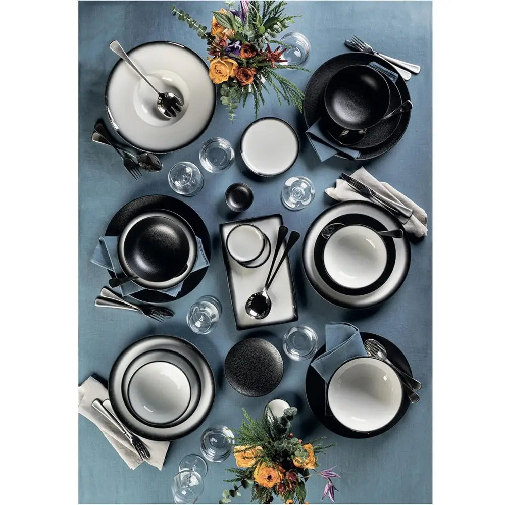Dining table setting with black and white dishes, silverware, and floral arrangements on a blue tablecloth.