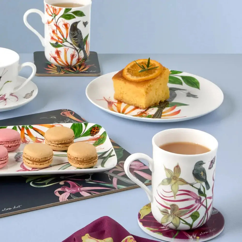 Tea set with floral mugs, cookies, and a cake on a light blue background