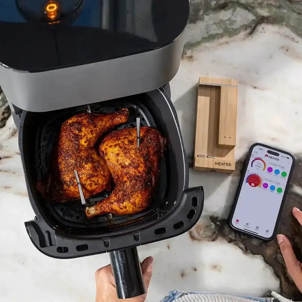 Air fryer with roasted chicken inside, smartphone app on marble countertop