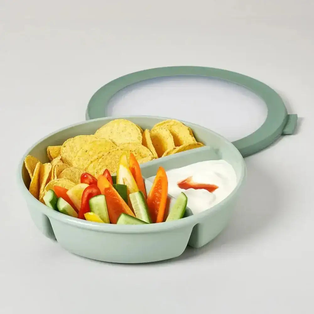 Green snack bowl with tortilla chips, vegetables, and dip on a light gray background