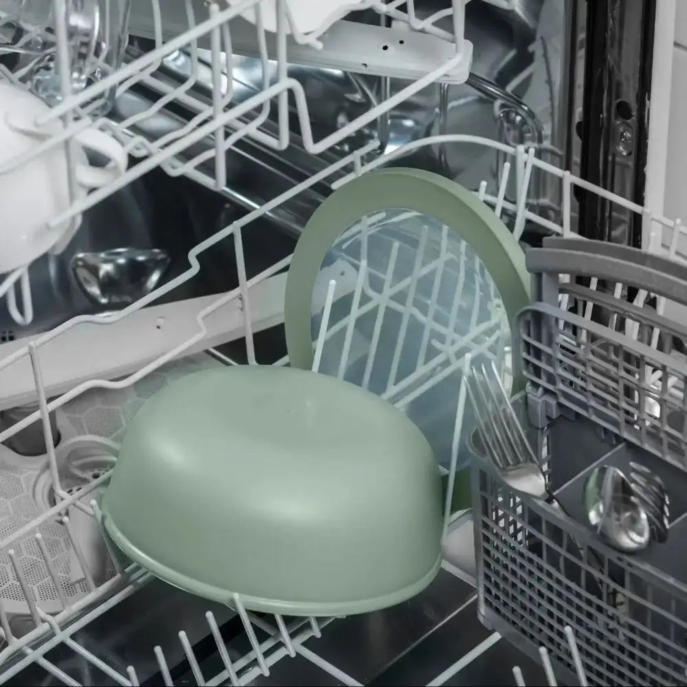 Green bowl inside an open dishwasher with silverware and other dishes.