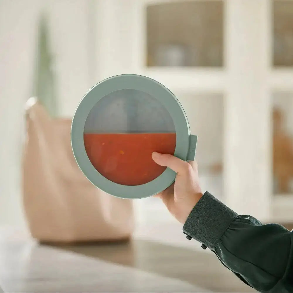 Person holding a round green object with a red interior in a blurred indoor setting