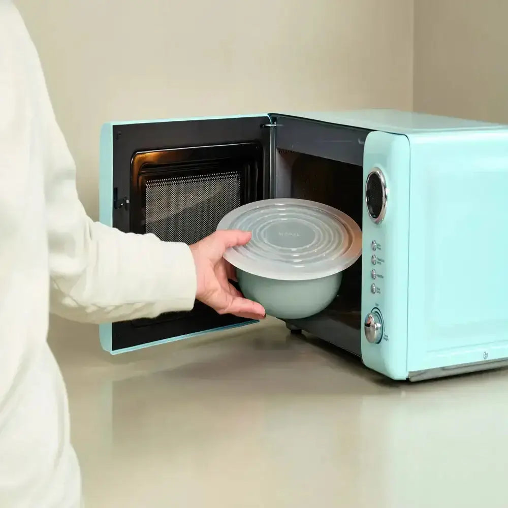 Person opening a teal microwave to place a green bowl with a lid inside.